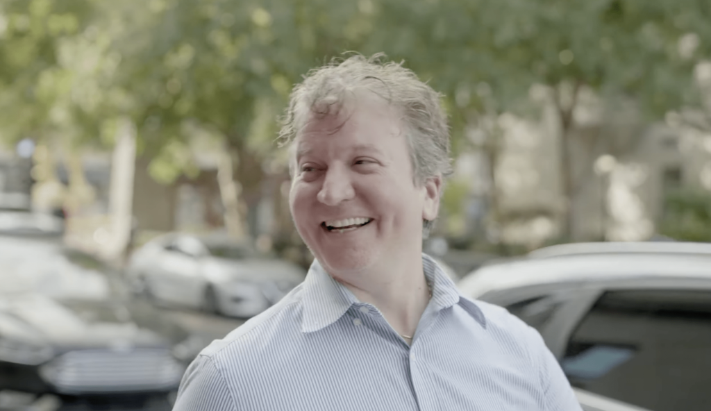 A smiling and laughing man walking down a sunny street